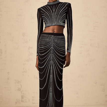 Woman wearing a black twopiece outfit consisting of a rhinestoneembellished mesh top and matching skirt