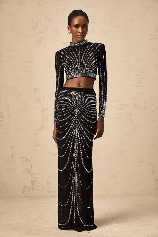 Woman wearing a black twopiece outfit consisting of a rhinestoneembellished mesh top and matching skirt