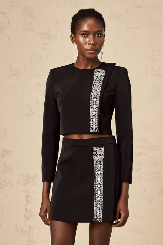 Woman wearing a black twopiece outfit consisting of a top and skirt adorned with crystal embellishments