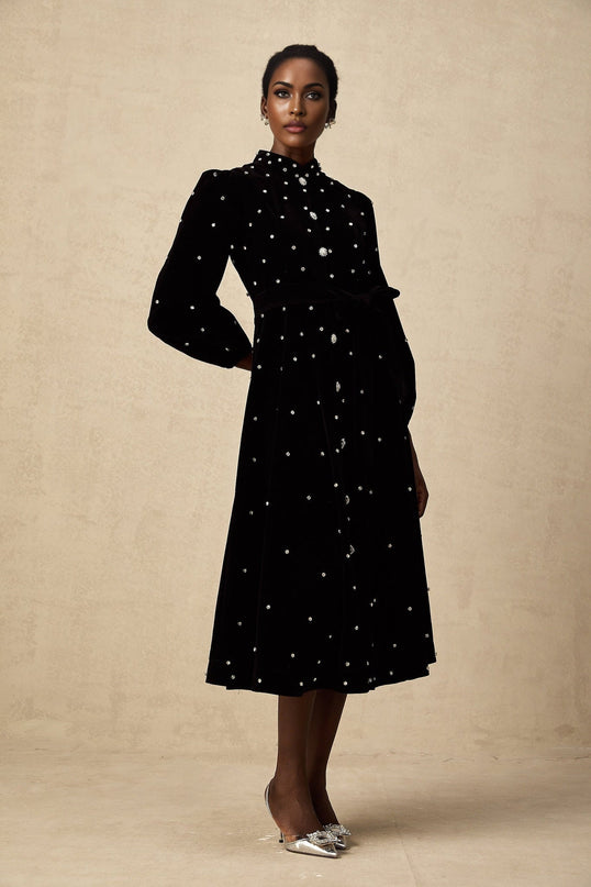Woman wearing a black velvet midi dress with embellishments and long sleeves