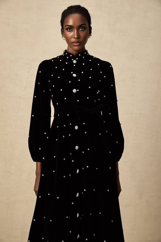 Woman wearing a black velvet midi dress with embellishments and slim fit silhouette