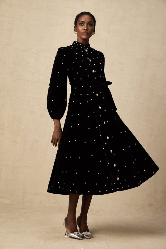Woman wearing a black velvet midi dress with embellishments standing against a plain background