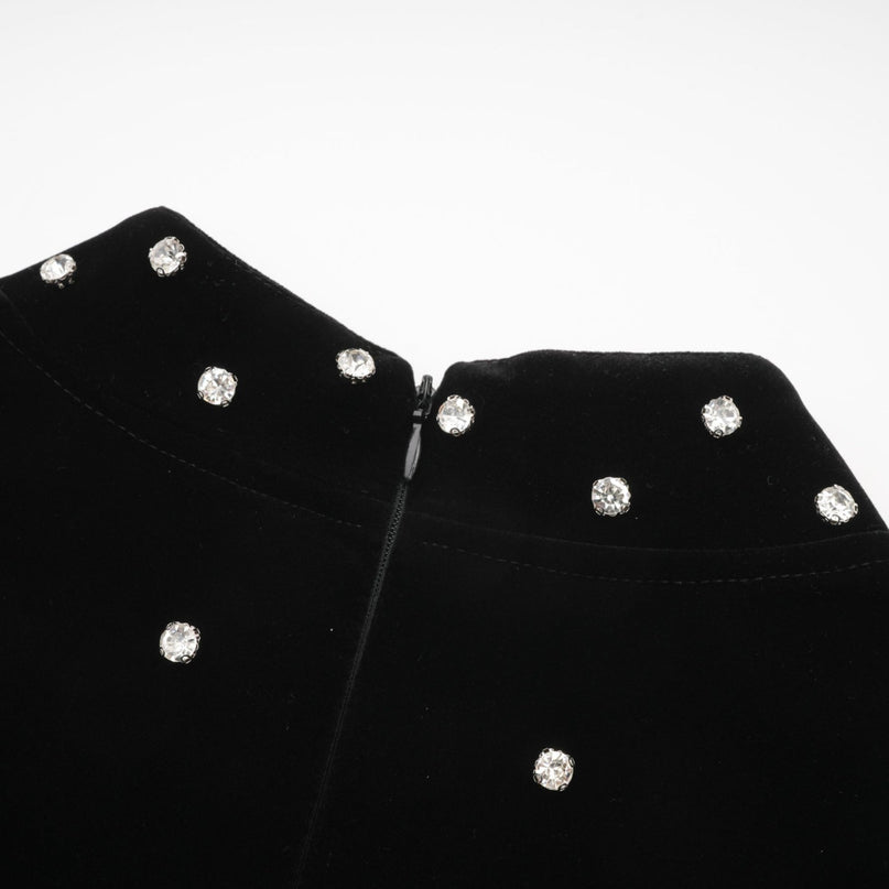 Woman wearing a black velvet midi dress with embellishments standing against a plain background