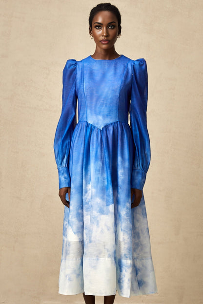 Woman wearing a blue gradient pleated midi dress with a flowing skirt and fitted bodice standing against a plain background
