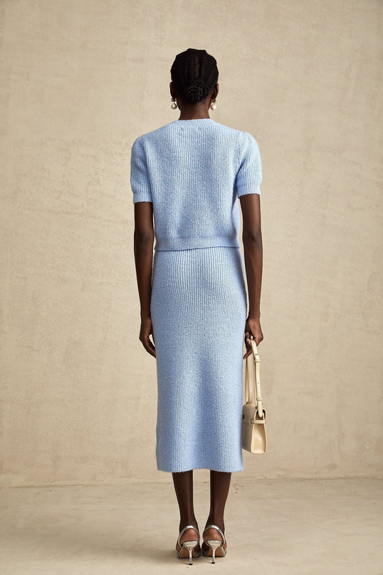 Woman wearing a blue knit blouse and matching skirt set against a plain background