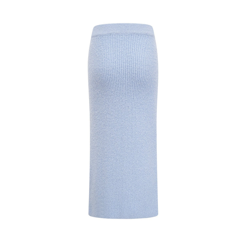 Woman wearing a blue knit matching set consisting of a blouse and skirt standing against a plain background