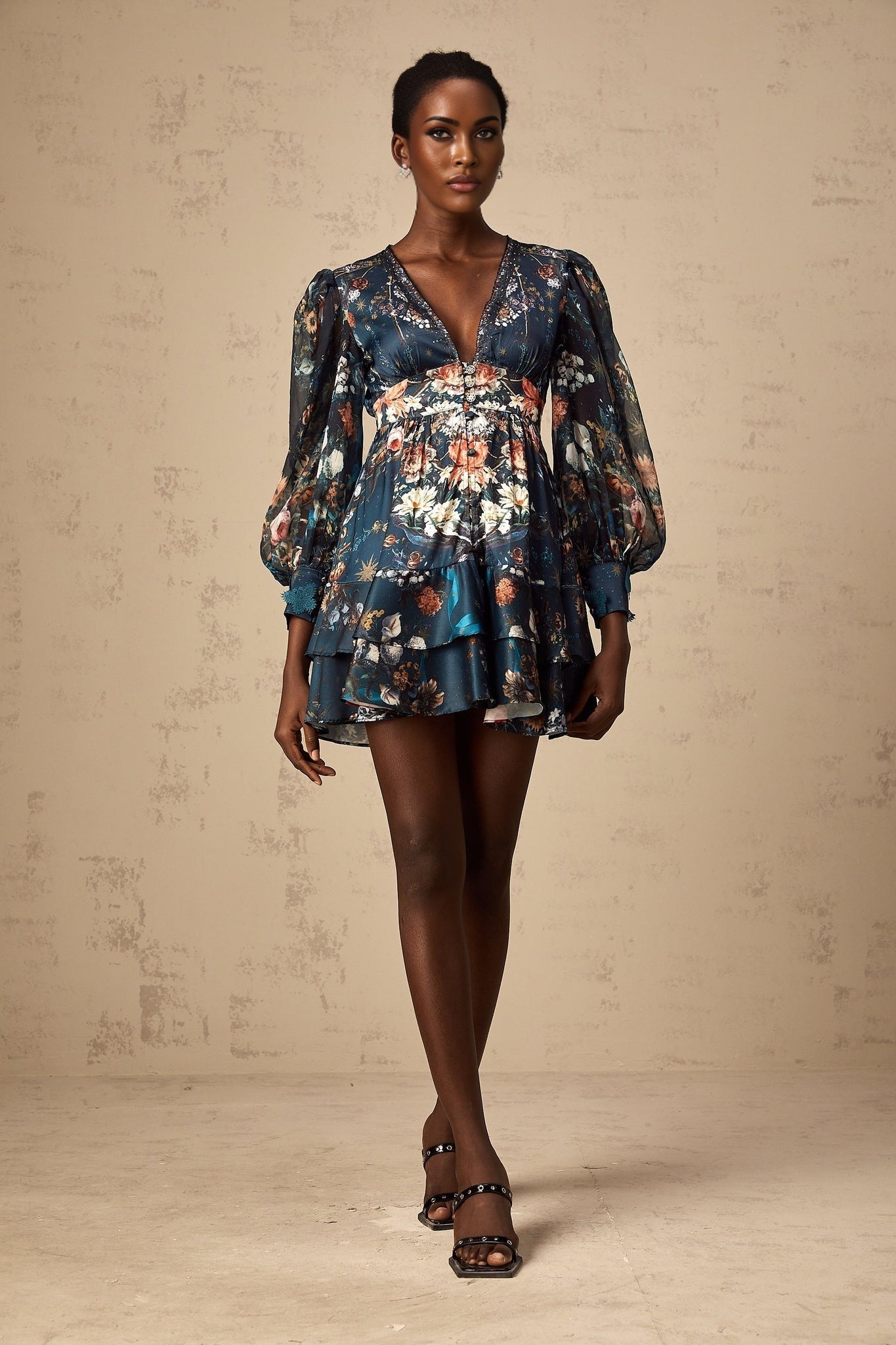 Woman wearing a blue mini dress with graphic print design and embellishments standing against a plain background
