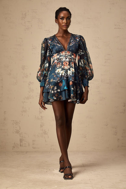 Woman wearing a blue mini dress with graphic print design and embellishments standing against a plain background