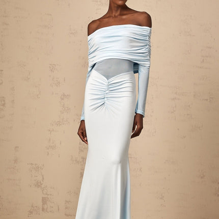 Woman wearing a blue offshoulder maxi dress with ruched detailing standing against a plain background