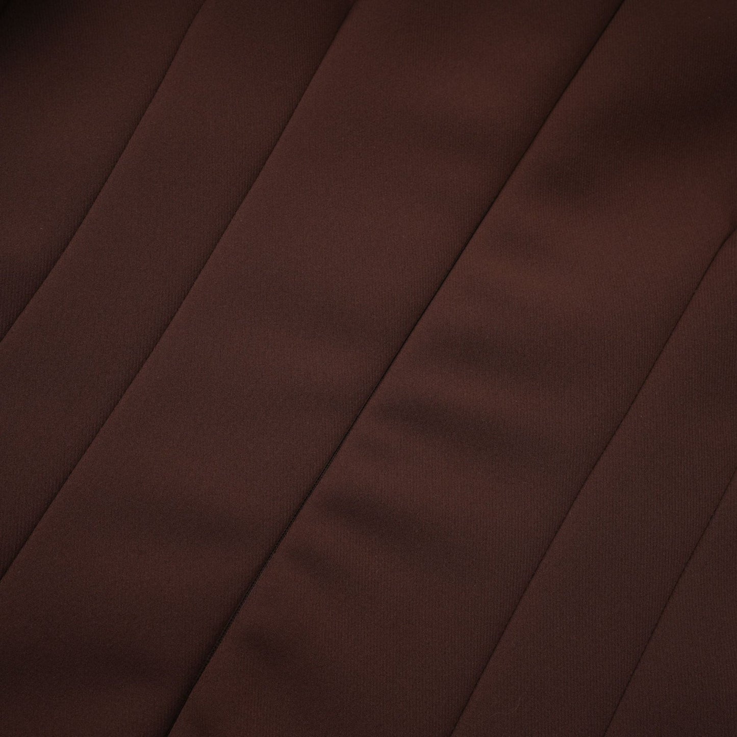 Woman wearing a brown asymmetrical midi dress with one shoulder design standing against a plain background