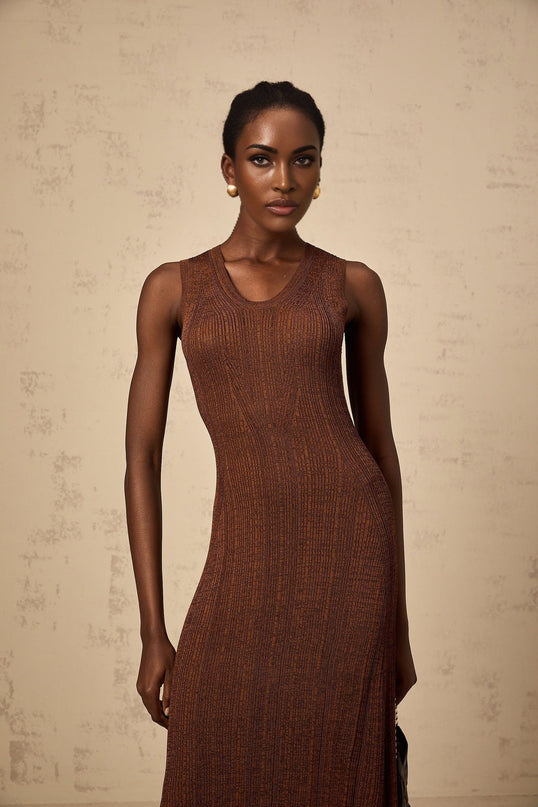 Woman wearing a brown knitted midi dress with cutout details standing in front of a plain background