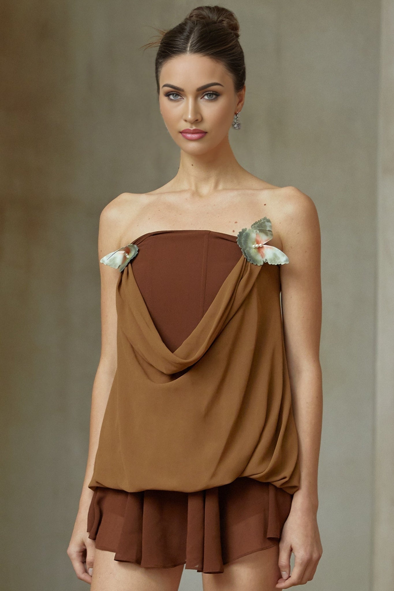 Woman wearing a brown twopiece outfit consisting of a panelled top and skirt adorned with butterfly pin details matching set