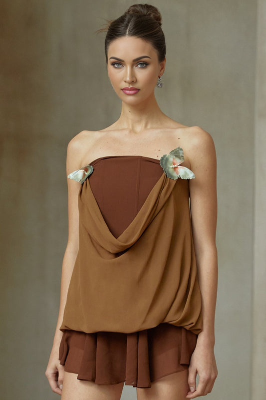 Woman wearing a brown twopiece outfit consisting of a panelled top and skirt adorned with butterfly pin details matching set