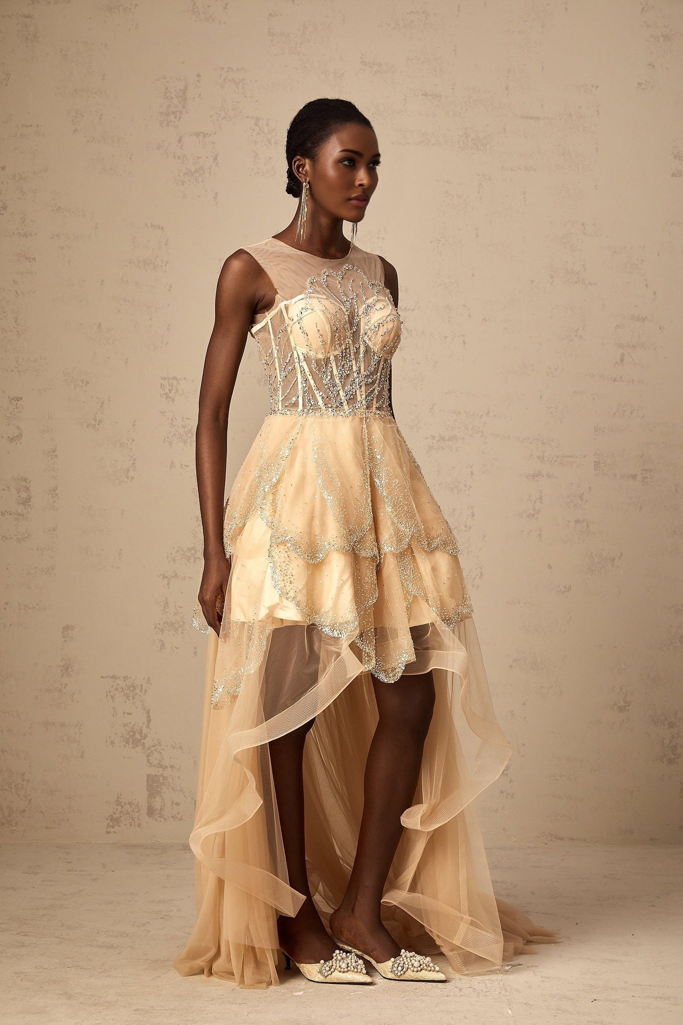 Woman wearing a champagne colored floor length gown with daisy floral embellishments and high low hemline