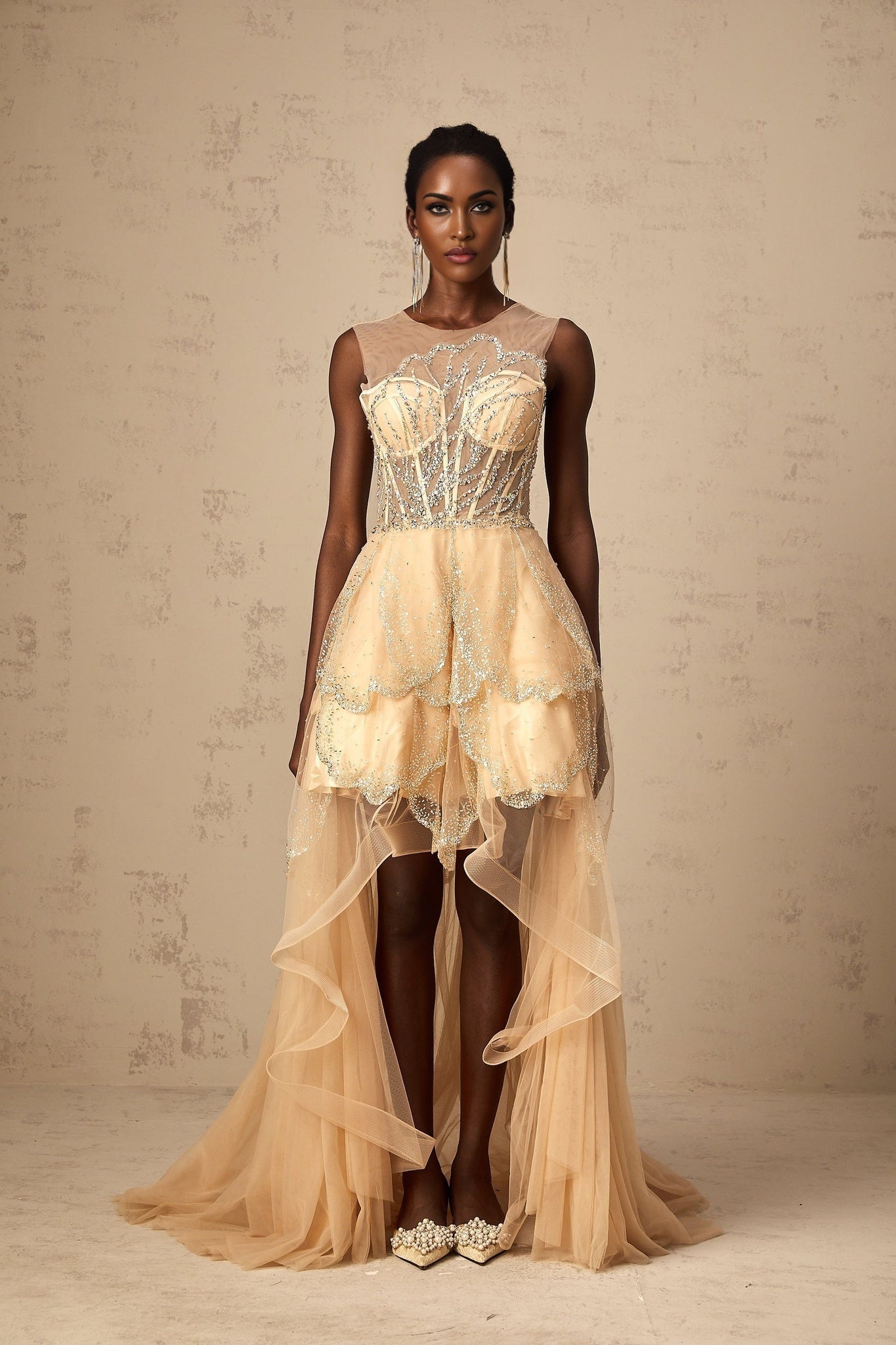 Woman wearing a champagne colored gown with daisy embellishments and high low hemline