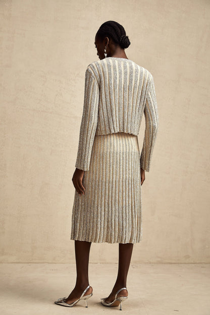 Woman wearing a champagne colored knit top and matching skirt with vertical stripes standing in a relaxed pose