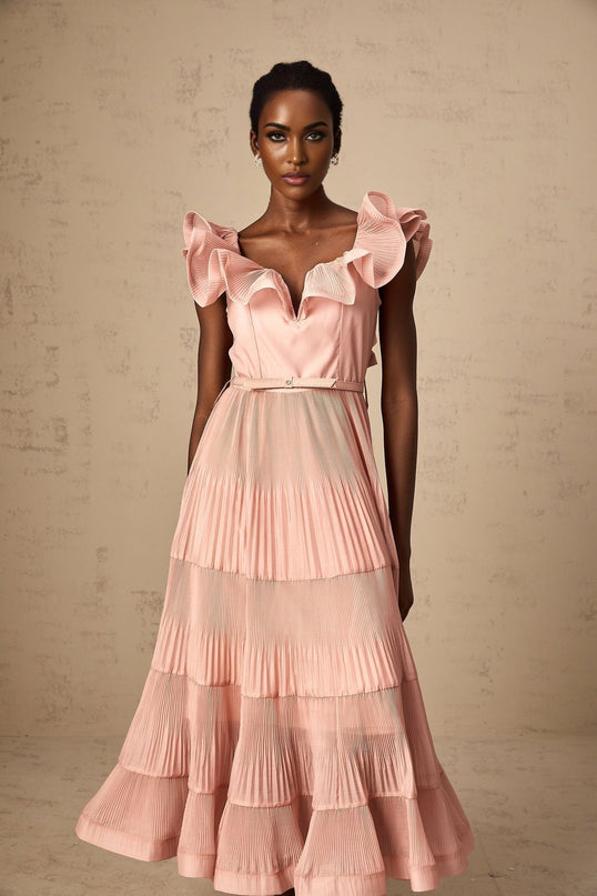 Woman wearing a coralpink midi dress with pleated fabric and frilly details standing in a neutral background