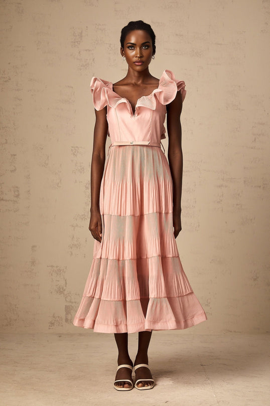Woman wearing a coralpink midi dress with pleated fabric and frilly details standing in a relaxed pose