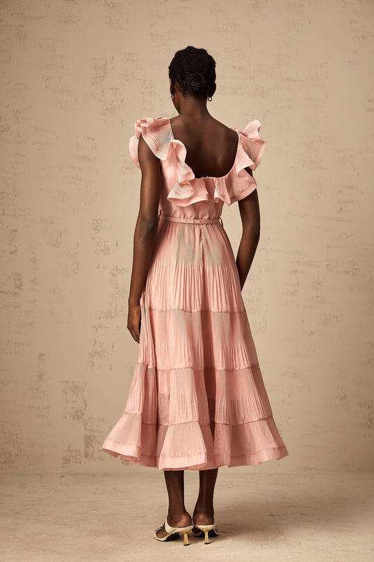 Woman wearing a coralpink midi dress with pleated frills and a flowy silhouette
