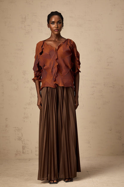 Woman wearing a demi brown matching set with creased texture top and skirt standing against plain background