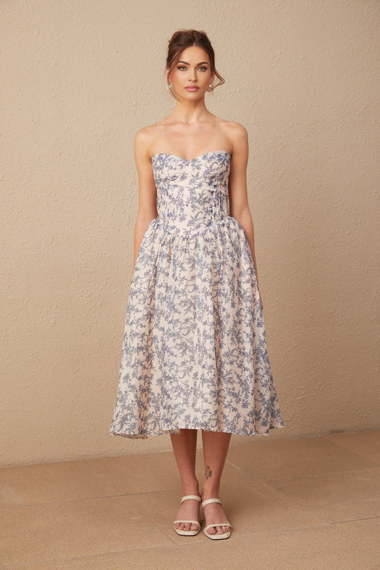 Woman wearing a floral print off shoulder midi dress with a fitted bodice and flared skirt in a garden setting