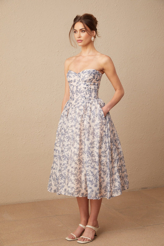 Woman wearing a floral print offshoulder midi dress with a fitted bodice and flared skirt in a garden setting