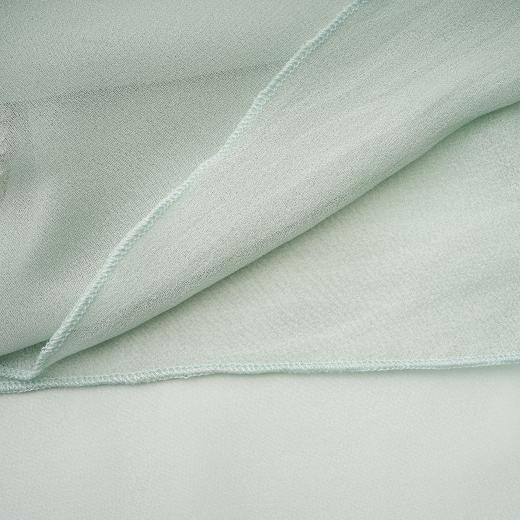 Woman wearing a flowy midi dress with ruffles and embellishments in a soft pastel color standing against a plain background