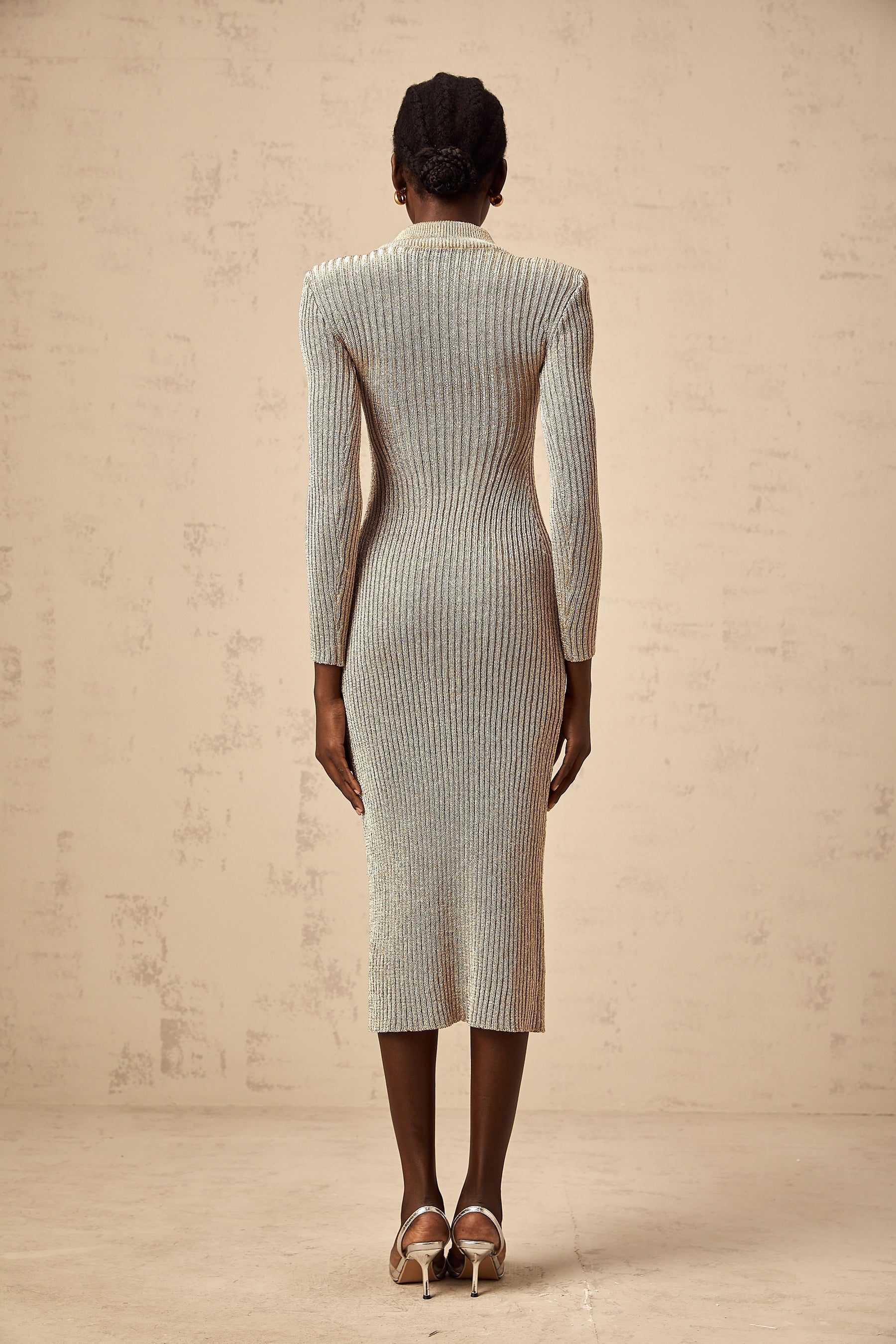 Woman wearing a gold ribbed knit midi dress with pointelle detailing standing in front of a plain background