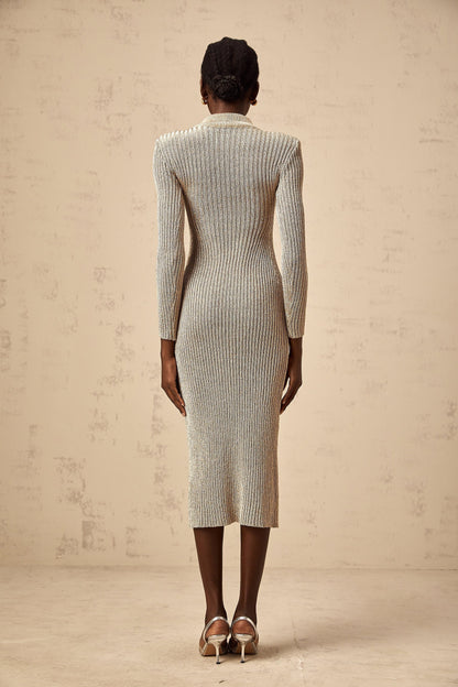 Woman wearing a gold ribbed knit midi dress with pointelle detailing standing in front of a plain background
