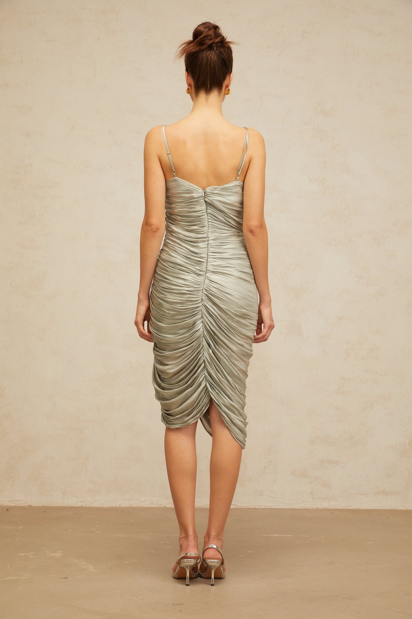 Woman wearing a grayish green glossy midi dress with ruched detailing fitted silhouette and sleek design