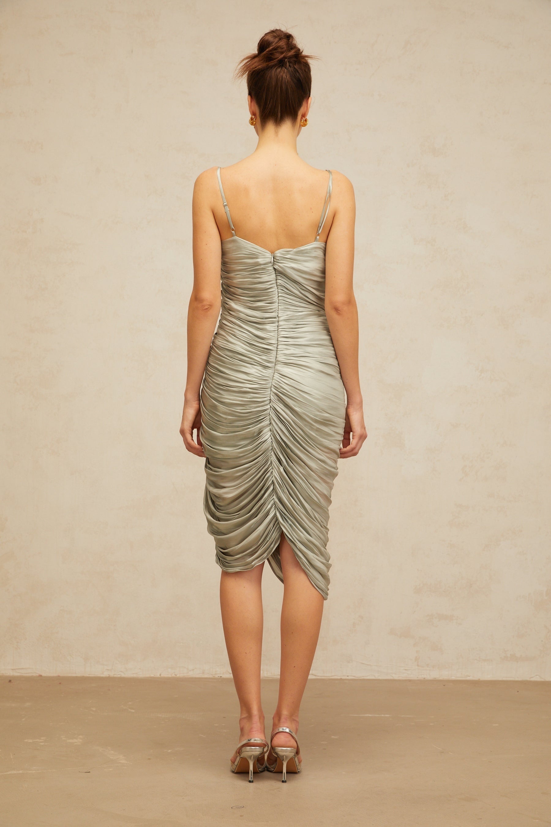 Woman wearing a grayish green glossy midi dress with ruched detailing fitted silhouette and sleek design