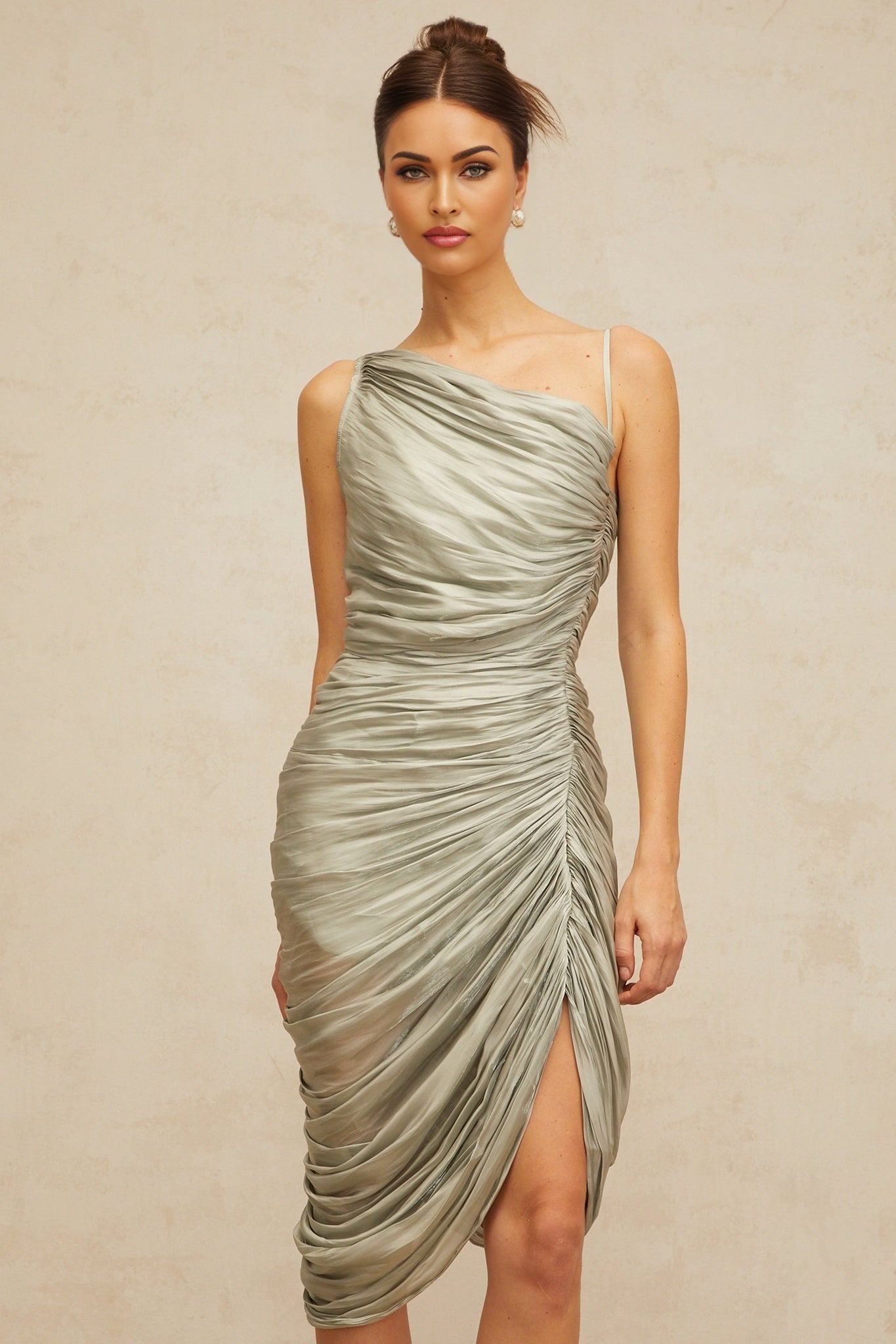 Woman wearing a grayish green glossy midi dress with ruched details standing in a neutral background