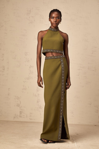 Woman wearing a green daisy print top and matching skirt with beaded trim details standing against a plain background
