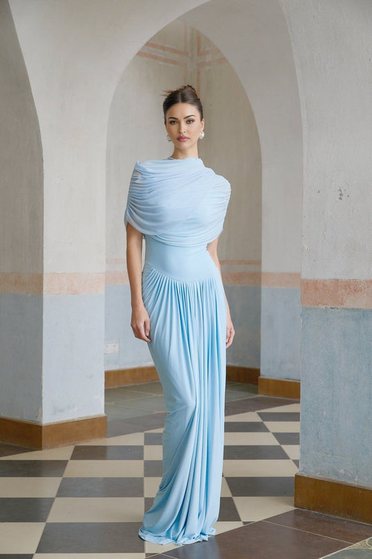 Woman wearing a light blue asymmetric pleated maxi dress with flowing fabric and elegant design