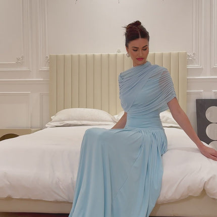 Woman wearing a light blue asymmetric pleated maxi dress with long sleeves and flowy skirt