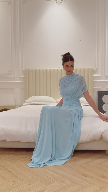 Woman wearing a light blue asymmetric pleated maxi dress with long sleeves and flowy skirt