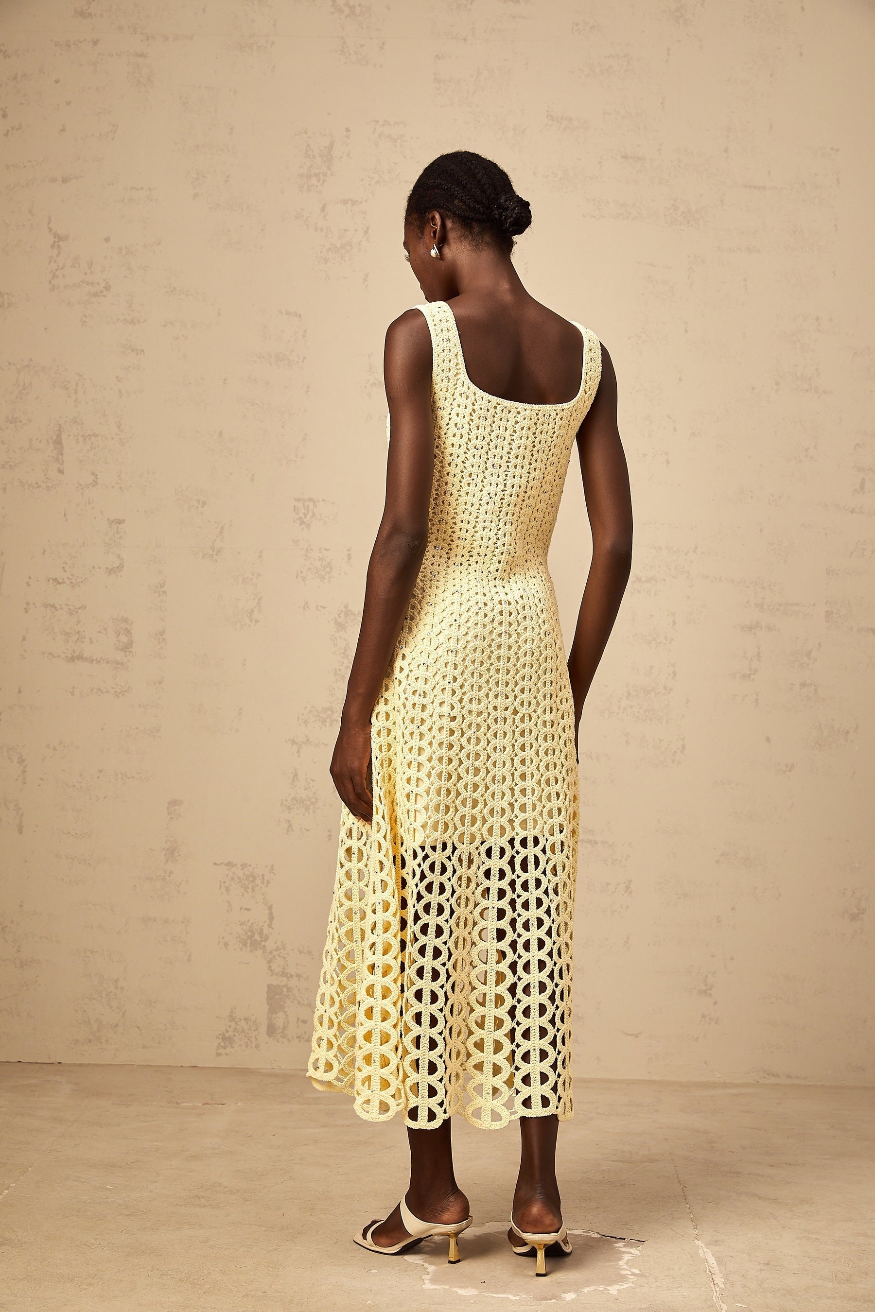 Woman wearing a light yellow crochet knit midi dress with embellishments and cutout details standing in a neutral setting