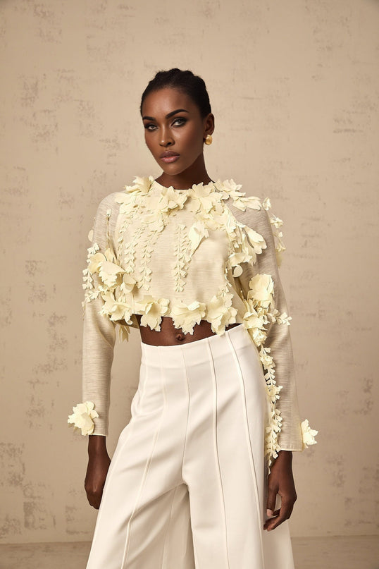 Woman wearing a light yellow cropped blouse with textured 3d petal details on the fabric