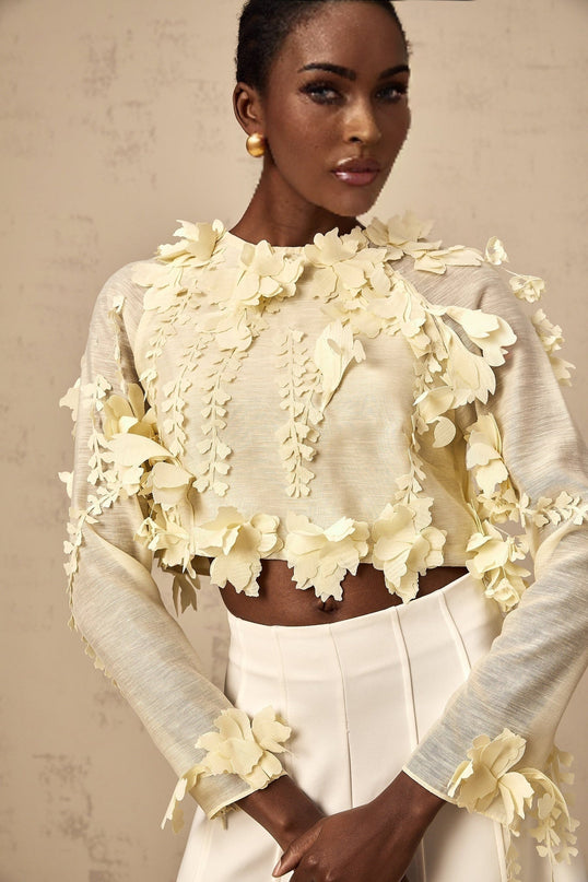 Woman wearing a light yellow cropped blouse with three dimensional floral petal details on the front