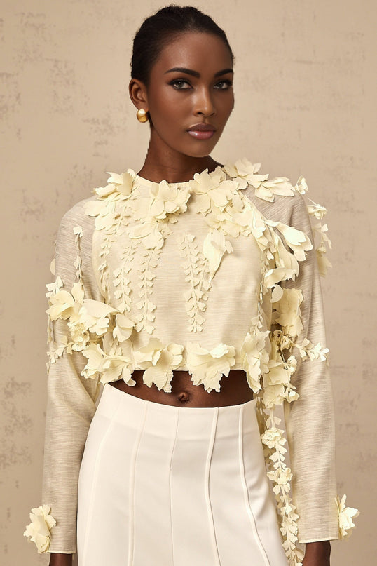 Woman wearing a light yellow cropped blouse with three dimensional petal details on the fabric
