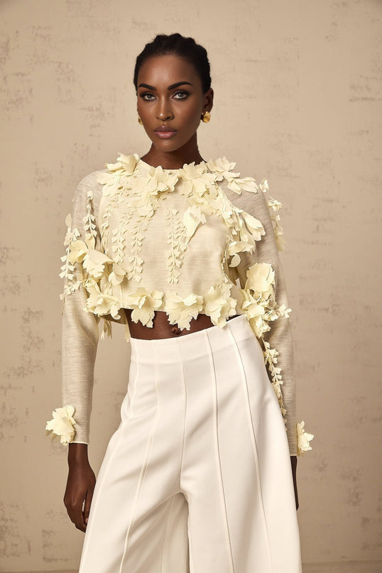 Woman wearing a light yellow cropped blouse with three dimensional petal details on the front