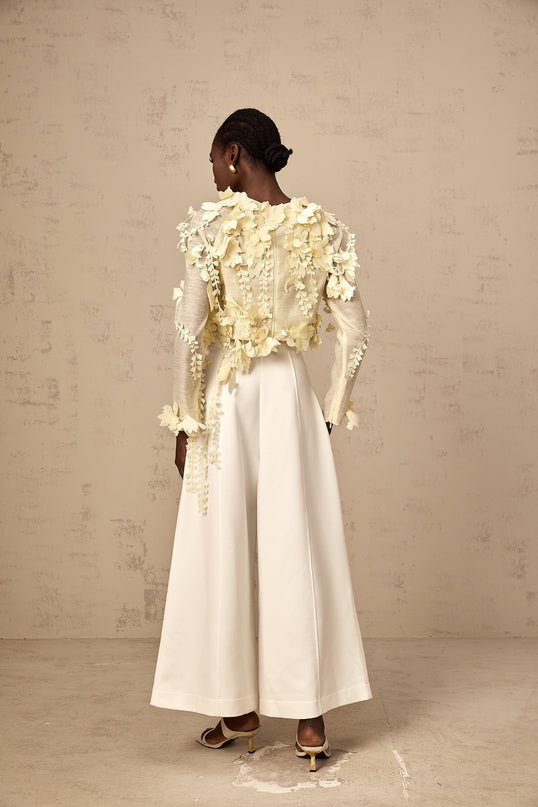 Woman wearing a light yellow cropped blouse with three dimensional petal details on the front