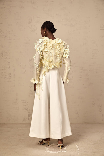 Woman wearing a light yellow cropped blouse with three dimensional petal details on the front