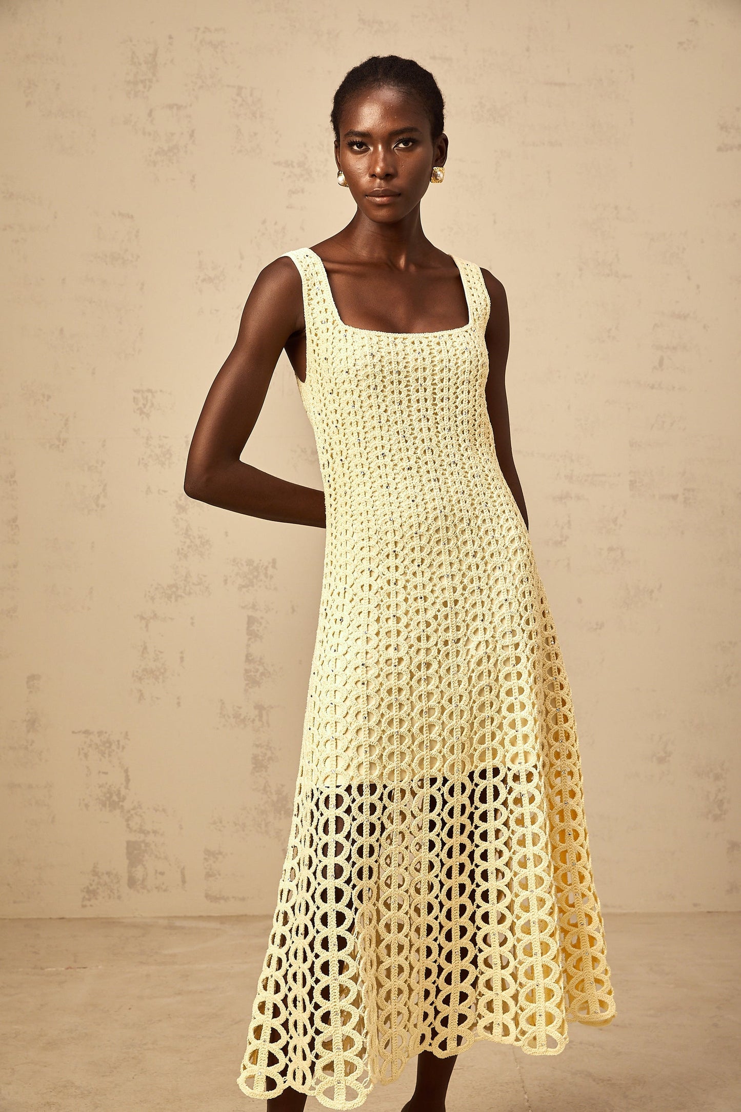 Woman wearing a light yellow midi dress with crochet knit pattern embellishments and cutout details