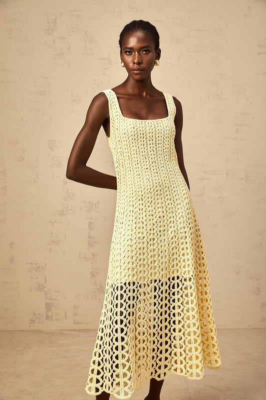 Woman wearing a light yellow midi dress with crochet knit pattern embellishments and cutout details