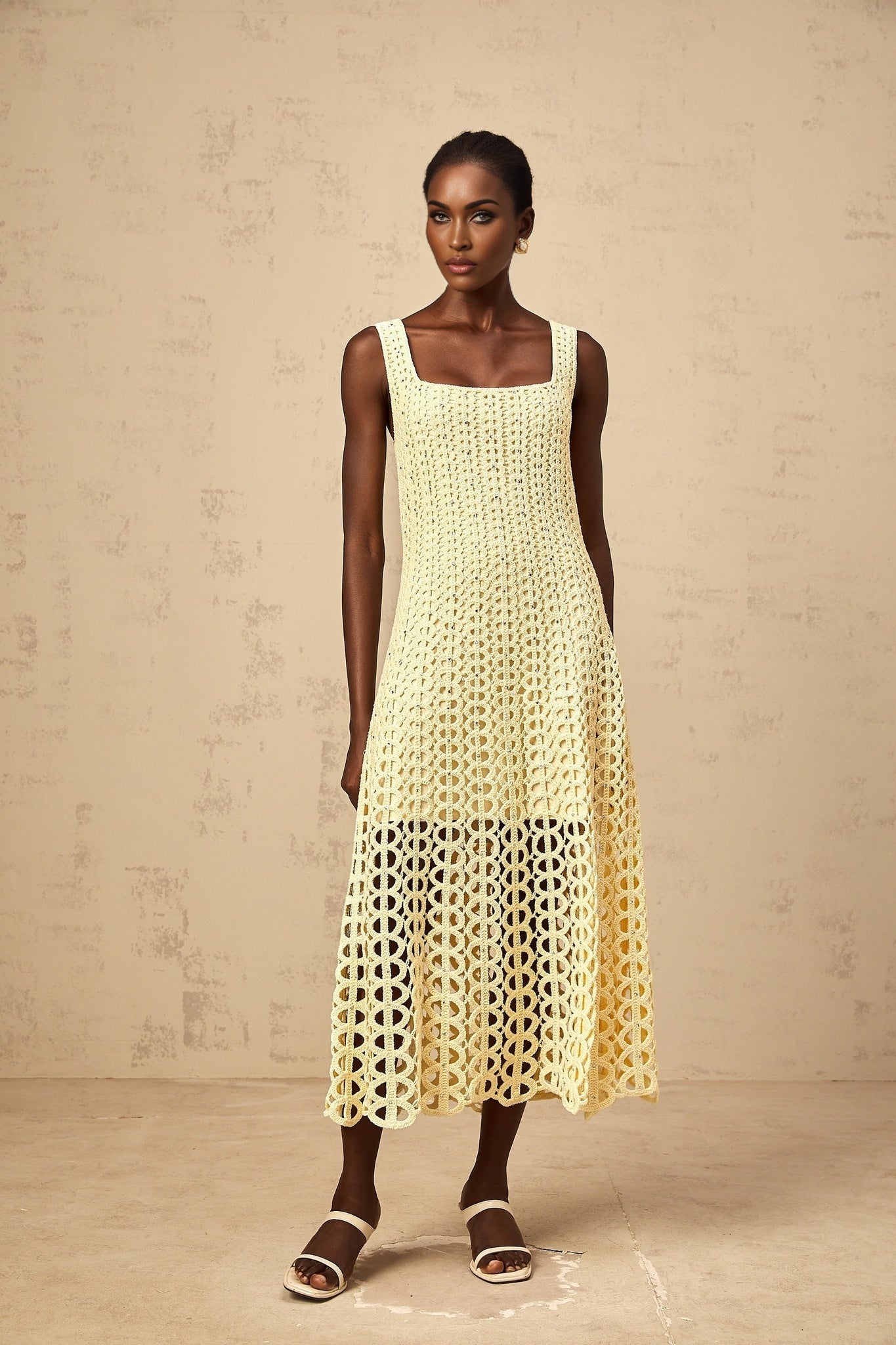Woman wearing a light yellow midi dress with crochet knit pattern featuring cutouts and embellishments