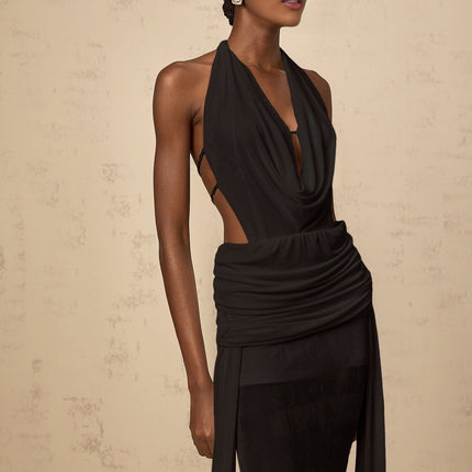Woman wearing a long black halterneck maxi dress with open back design standing against plain background