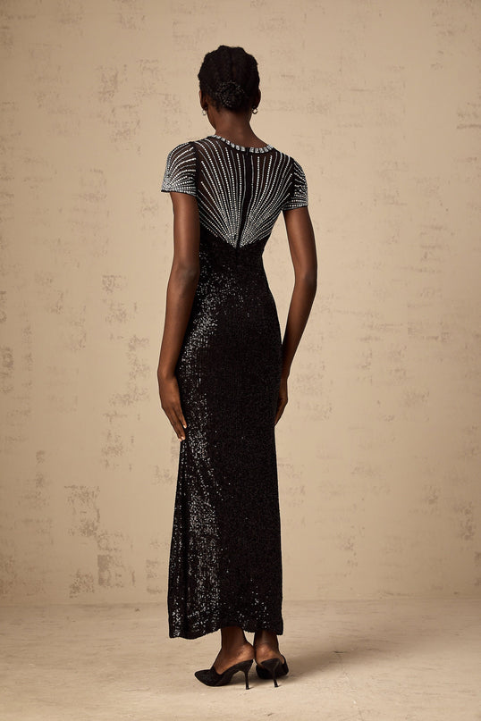 Woman wearing a long black sequined maxi dress with cut out details