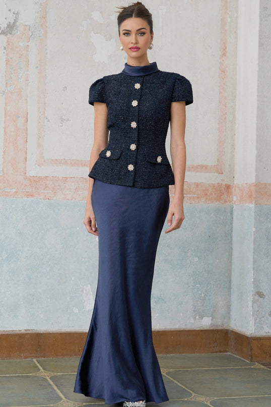 Woman wearing a long blue maxi dress with a fitted peplum waist and panelled design standing in a neutral background