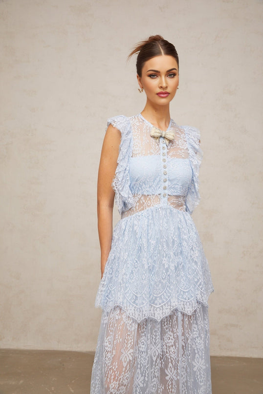 Woman wearing a long blue maxi dress with layered lace details and capucine color accents